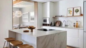 Una cocina moderna con una isla de mármol, taburetes de bar, microondas y un fregadero.