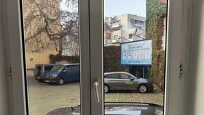 Vista a través de una puerta con dos paneles de vidrio, mostrando un estacionamiento con coches y un edificio con un letrero que dice "DIGITALIZI/TE".