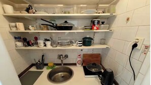 Cocina compacta con azulejos blancos, un lavamanos de acero inoxidable, una estufa y diversos utensilios y electrodomésticos.