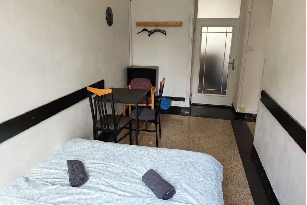 Une petite pièce étroite, avec un lit, une table et deux chaises.
