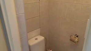 Un baño pequeño y limpio con inodoro, dispensador de papel higiénico y un pequeño cubo de basura.