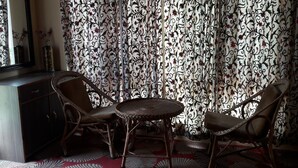 A room with a dark wooden cabinet, two wicker chairs, a small round table, and a patterned curtain. - Blooming Dale (Srinagar)