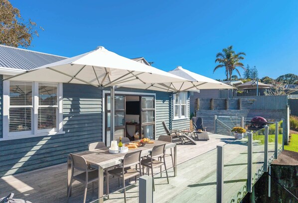 A covered outdoor patio with a table and chairs, a grill, and a view of a residential area.