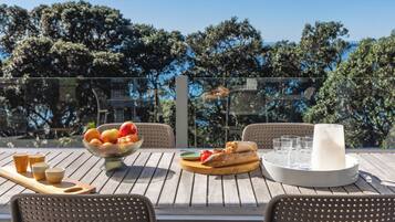 An outdoor dining area with a table set for four, including a fruit bowl, a plate of bread, and glasses.