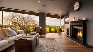 Un salon moderne comprenant un canapé, une table basse, une cheminée et de grandes fenêtres donnant sur la campagne.
