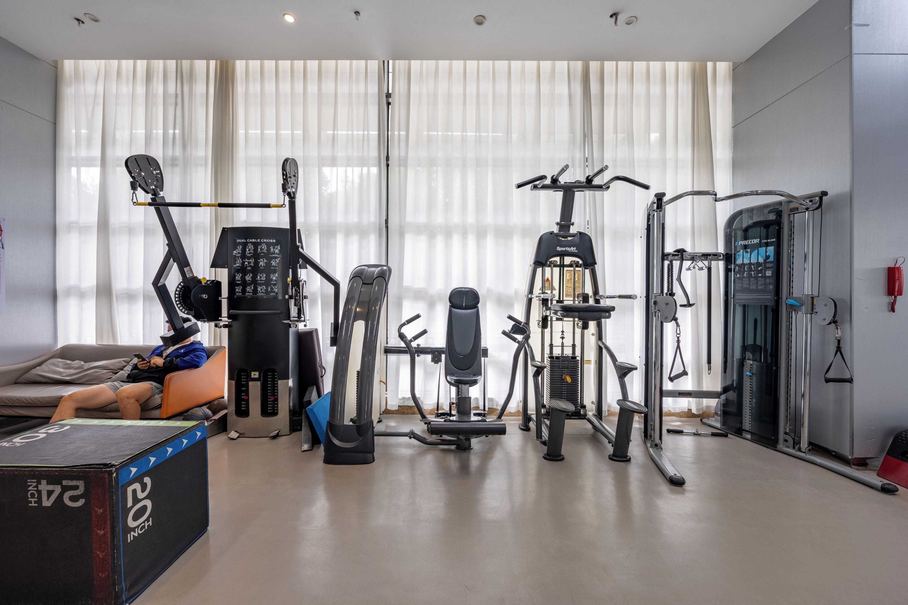 A home gym with various exercise equipment, a sofa, and a large window with curtains.