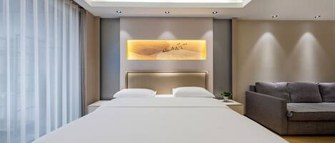 A modern hotel room with a large bed, a sofa, a wall-mounted artwork, and a skylight.