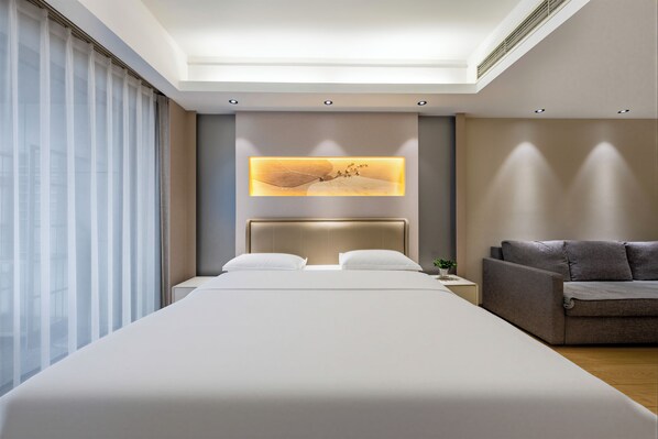 Una habitación de hotel moderna con una cama grande, un sofá, una obra de arte en la pared y un tragaluz.