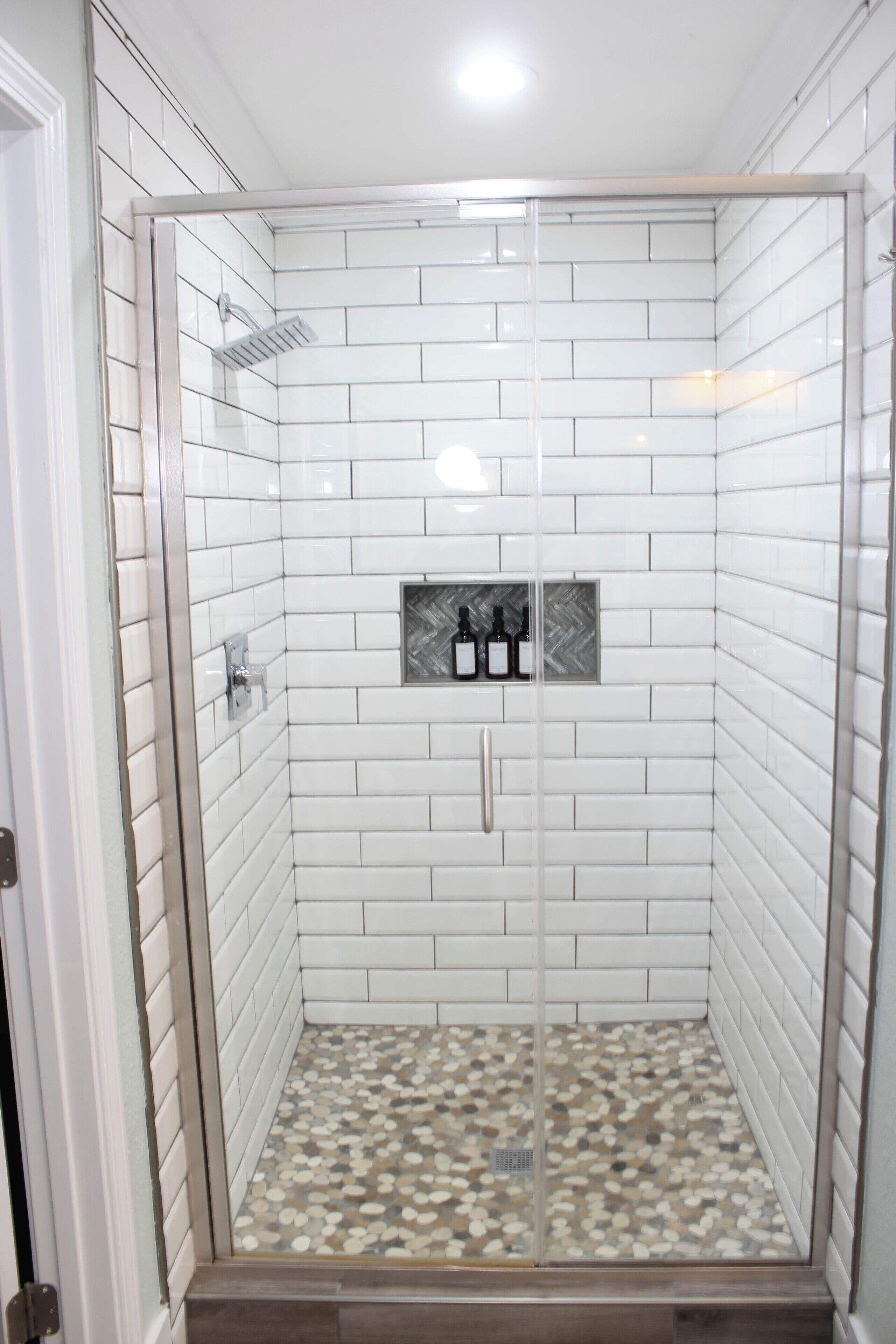 Une douche à l’italienne avec des carreaux de céramique blancs rectangulaires et un sol à motifs de galets.