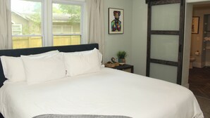 Un dormitorio con una cama grande, una ventana, un cuadro y una puerta corredera que da a otra habitación.