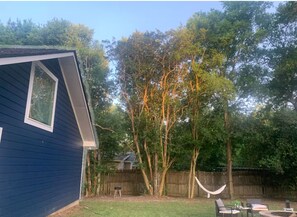 Un cortile con una casa blu, un'amaca, un barbecue e una recinzione in legno.