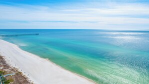 Une plage à l’eau turquoise et limpide, une jetée qui s’avance dans la mer et un ciel dégagé.
