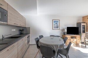 Et moderne køkken med indbygget komfur, spiseplads med rundt bord og et fladskærms-tv på et træskab.