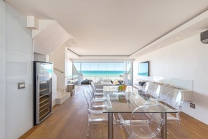 Une cuisine moderne avec une table et des chaises en verre, un four encastré et une vue sur l’océan.
