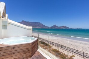 A wooden deck with a hot tub overlooking a beach and mountains.