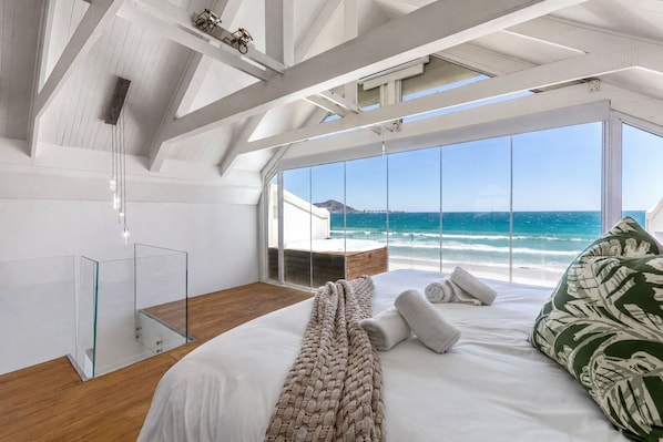 A bedroom with a large bed, a view of the ocean, and a wooden ceiling structure.
