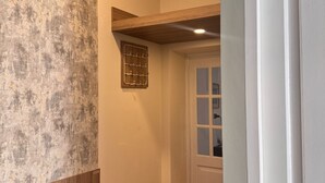 Un couloir avec un mur à texture, une étagère en bois, une porte avec des panneaux de verre et un sol carrelé.