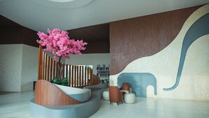 Eine moderne Lobby mit einer gebogenen Sitzecke, einem Holzbüro und einem großen blühenden Baum in Rosa.