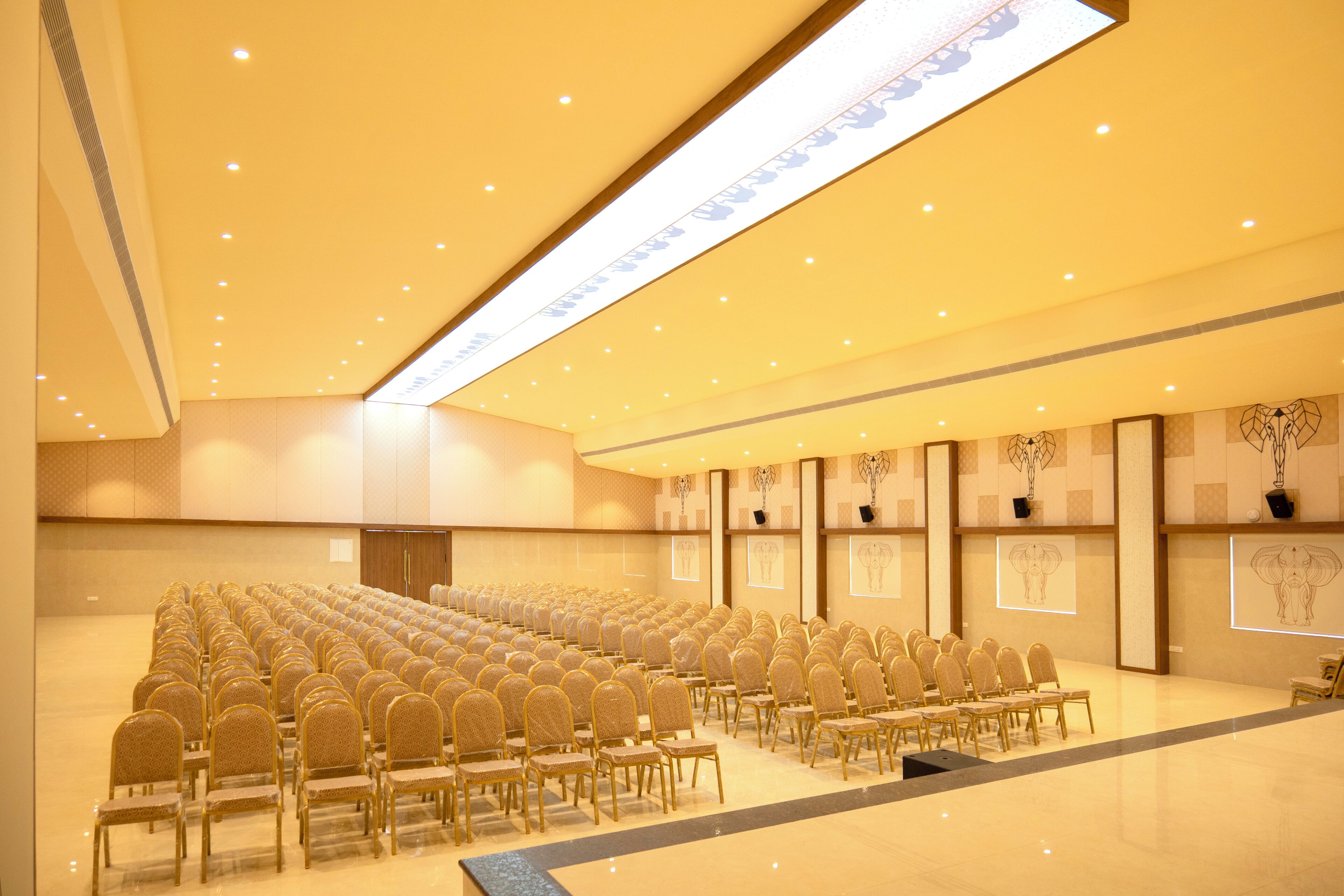 A conference room with rows of chairs, a high ceiling with recessed lighting, and framed artwork on the walls.