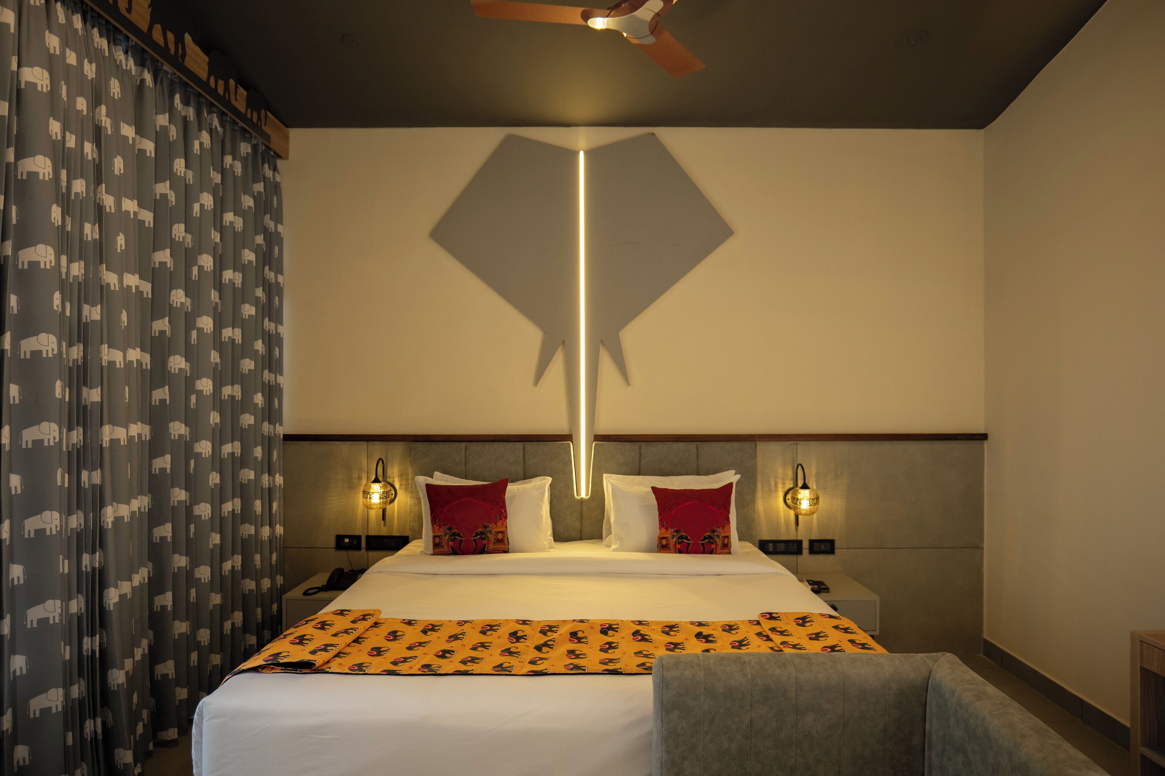 A hotel room with a large bed, two bedside tables, a ceiling fan, and patterned curtains.