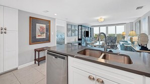 A modern kitchen with a dishwasher, a sink, and a dining area with a blue cabinet and a table. - Anchorage Resort 8th floor condo in Siesta Key with private beach access, pool, (Siesta Key)