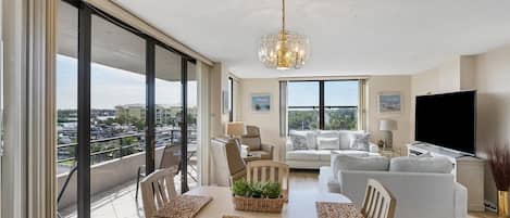 A spacious living area with a balcony, large windows, and a modern chandelier.