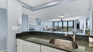 A modern kitchen with a granite countertop, stainless steel sink, and white cabinetry.