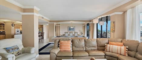 Un salón espacioso con un amplio sofá en forma de L, una zona de comedor con mesa de billar y una cocina al fondo.