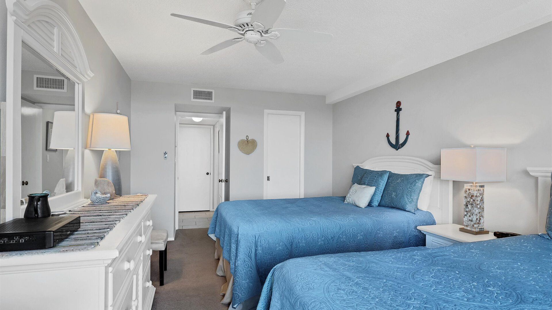 Une chambre avec deux lits, un ventilateur de plafond, une commode et une lampe.