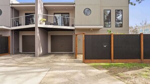 A modern two-story building with a balcony, garage doors, and a fenced area. - Stylish Townhouse 2 Min Walk to Beach & Shops (Cowes)