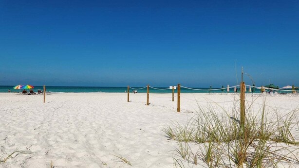 A beach with a rope barrier, a few beach chairs, and a colorful umbrella.