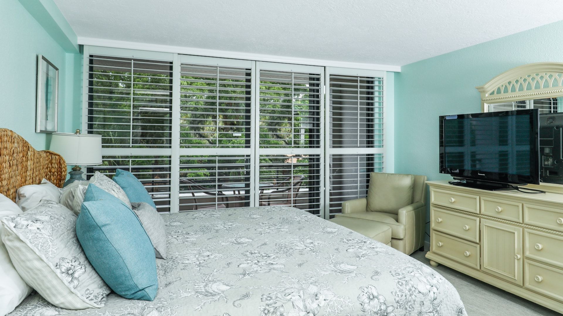A bedroom with a large bed, a television, a dresser, and a window with blinds.
