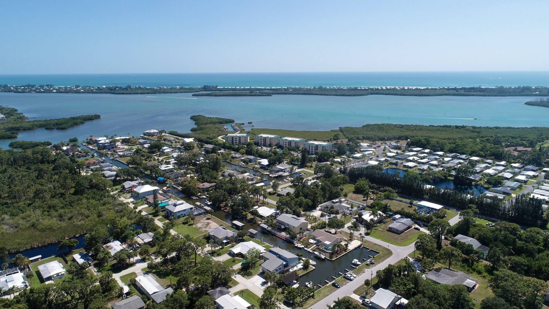 Vista aérea de una zona residencial costera con varios edificios, un puerto deportivo y una gran masa de agua.