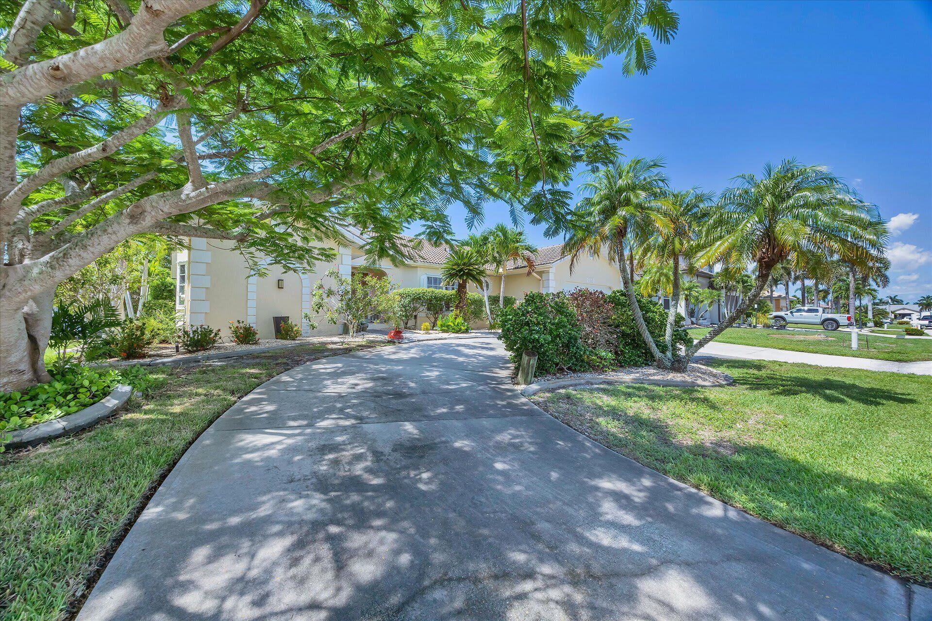 A residential street with houses, palm trees, and a clear sky.