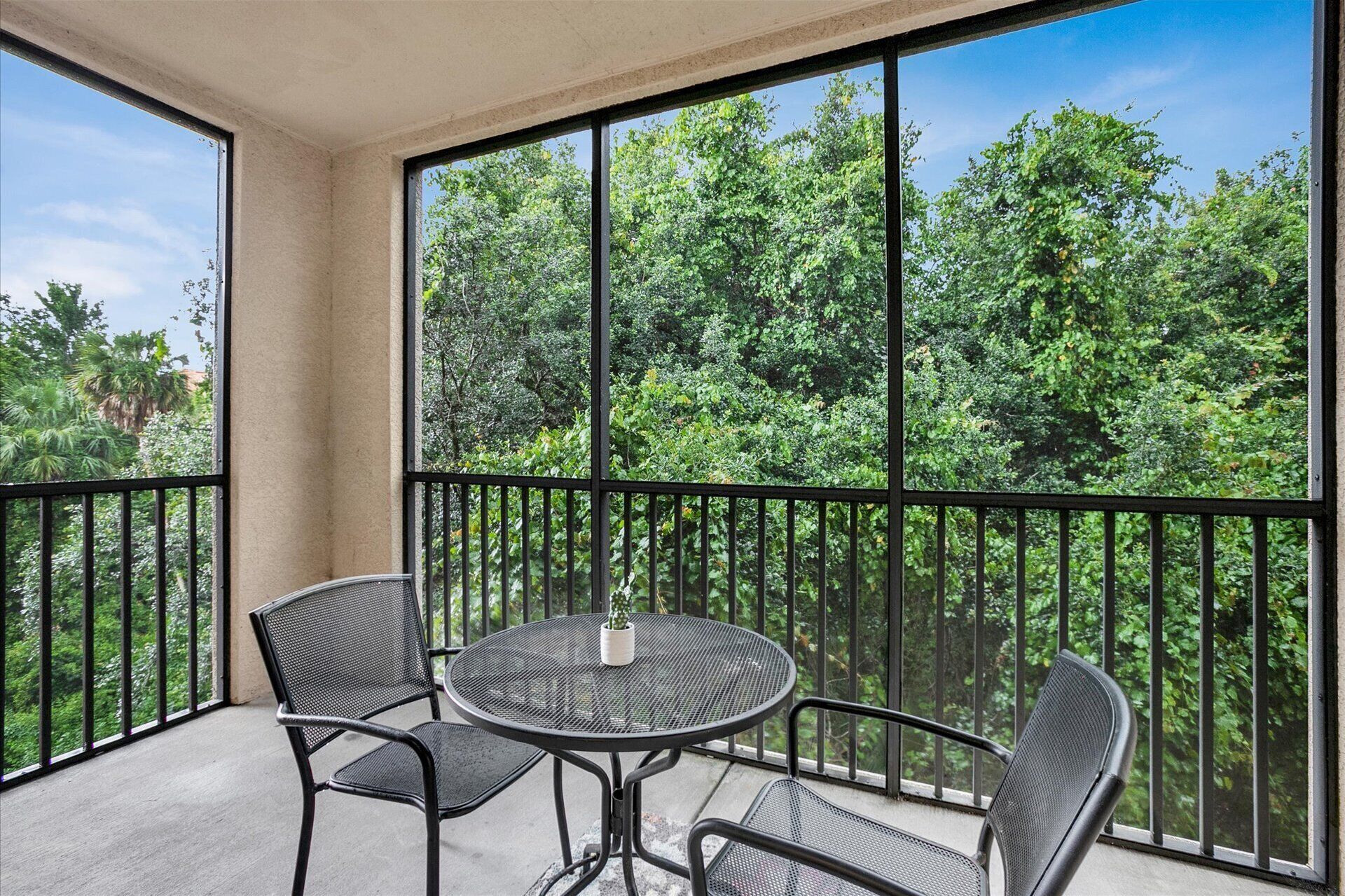 A balcony with a round table and two chairs, overlooking a lush green forest.
