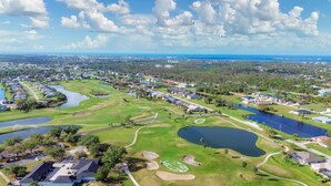 Luchtbeeld van een golfbaan met meerdere vijvers, een clubhuis en woonwijken op de achtergrond.