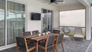 A patio with a wooden table and chairs, a ceiling fan, and a large window. - Windsor Island Resort 5 Bedroom East Facing Pool - P820923 (Davenport)