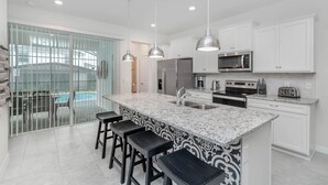 A modern kitchen with a large island, stainless steel appliances, and a view of a pool.