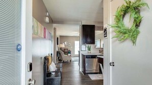 A hallway with a modern kitchen area, a dining area with a chair and table, and a decorative wreath on the wall. - Loft #211 (540 N 2nd St) (Clarksville)