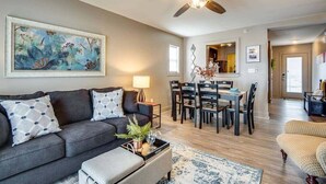 A living room with a dark grey sofa, a coffee table, and a ceiling fan. There is a dining area with a wooden table and chairs. - Loft #211 (540 N 2nd St) (Clarksville)