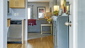 A hallway with wooden flooring, a kitchen area with wooden cabinets, a dining area with a table and chairs, and a living room with a sofa and a fireplace. - Loft #304 (540 N 2nd St) (Clarksville)