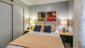A neatly arranged hotel room with a bed, two bedside tables, and two wall-mounted paintings. - Loft #304 (540 N 2nd St) (Clarksville)