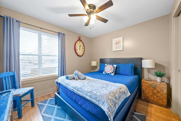 A bedroom with a bed, a ceiling fan, a clock, a bedside table with a lamp, and a window with curtains. - Loft #105 (540 N 2nd St) (Clarksville)