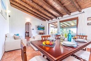 A dining area with a wooden table set for two, a television mounted on the wall, and a view of the outdoors through a glass door. - Villa La Licciola (Arzachena)