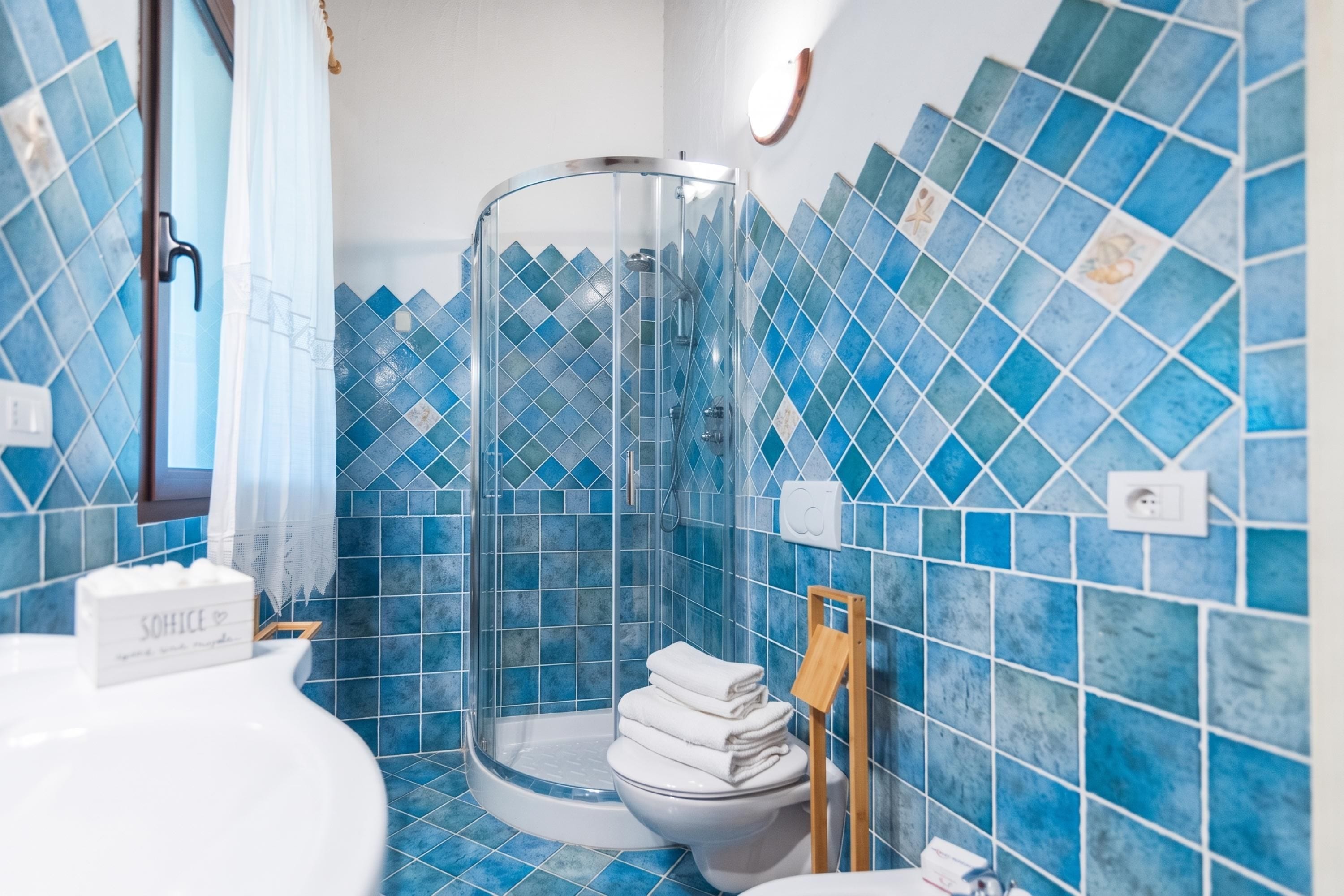 A bathroom with a glass shower enclosure, a toilet, and blue-tiled walls.
