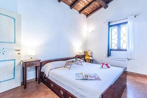 Un dormitorio con cama de madera, mesitas de noche, una ventana con cortinas y suelo de baldosas.