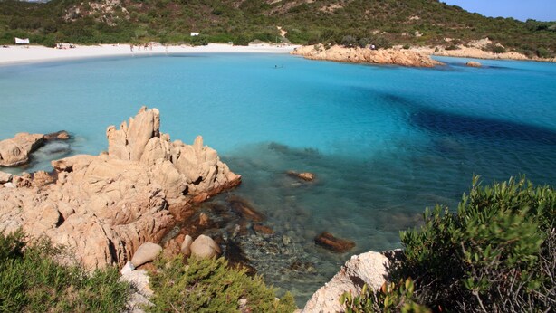 A coastal landscape with clear turquoise waters, rocky formations, and a sandy beach.