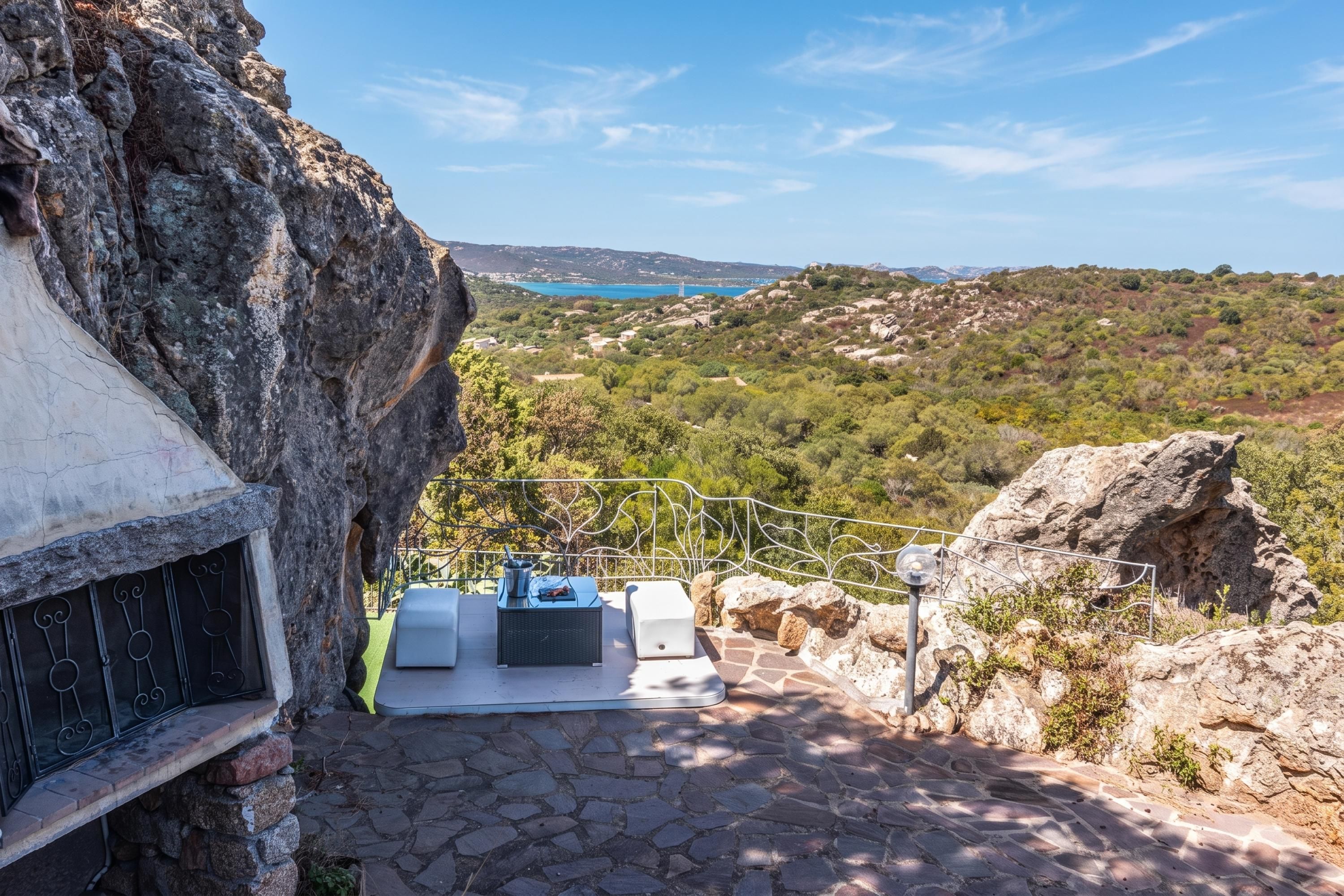 A stone staircase leading to a terrace with outdoor seating and a view of a coastal landscape.