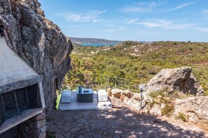 A stone staircase leading to a terrace with outdoor seating and a view of a coastal landscape.