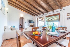 Un comedor con una mesa de madera, sillas y un televisor al fondo.